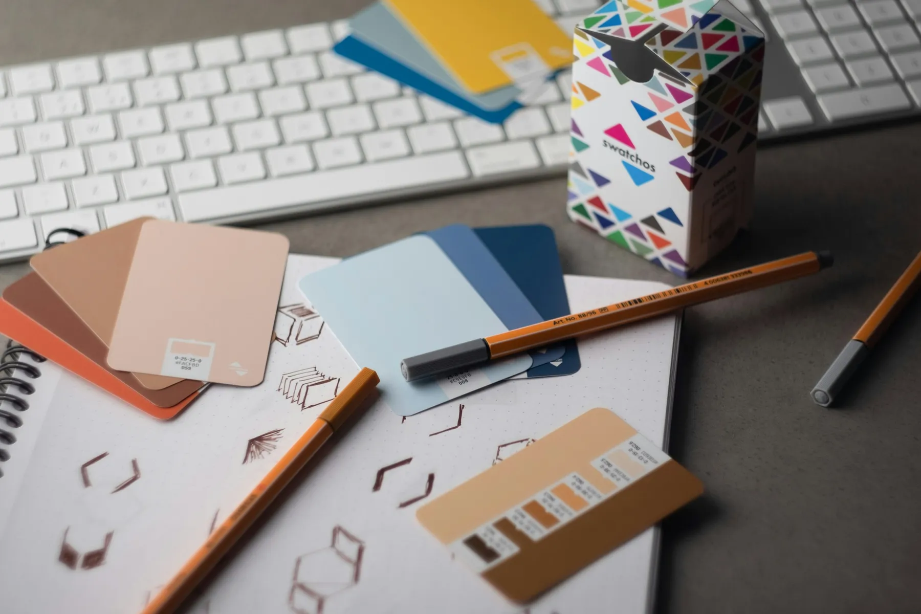 Colour swatches, pencils and a sketchbook of hand-drawn logo marks on a studio desk