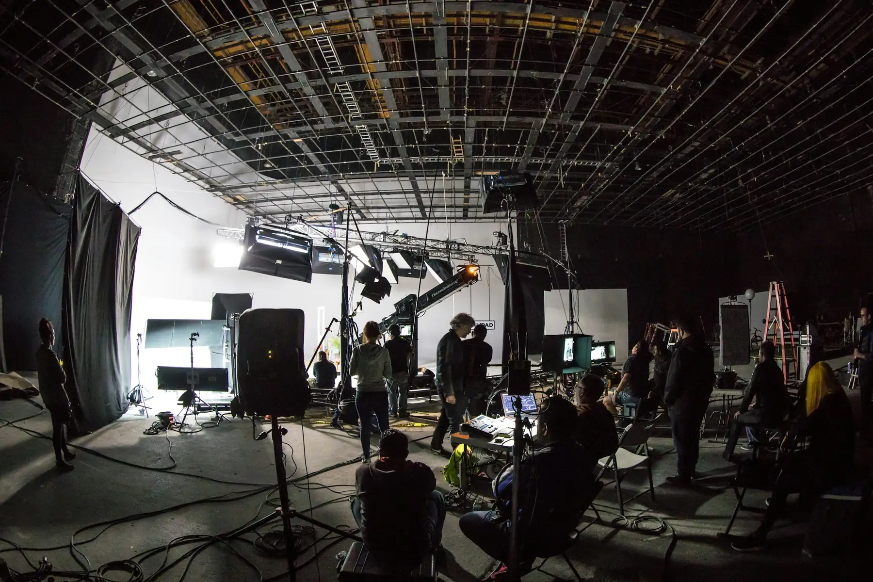 A film crew working on a large soundstage surrounded by lighting rigs and cameras