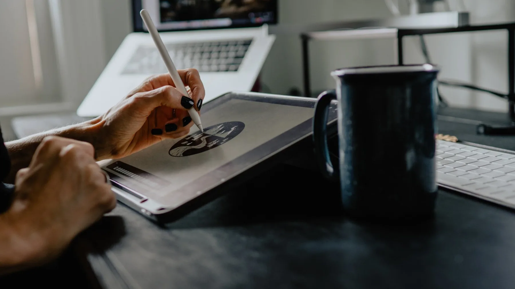 A designer drawing a logo mark on a graphics tablet beside a laptop